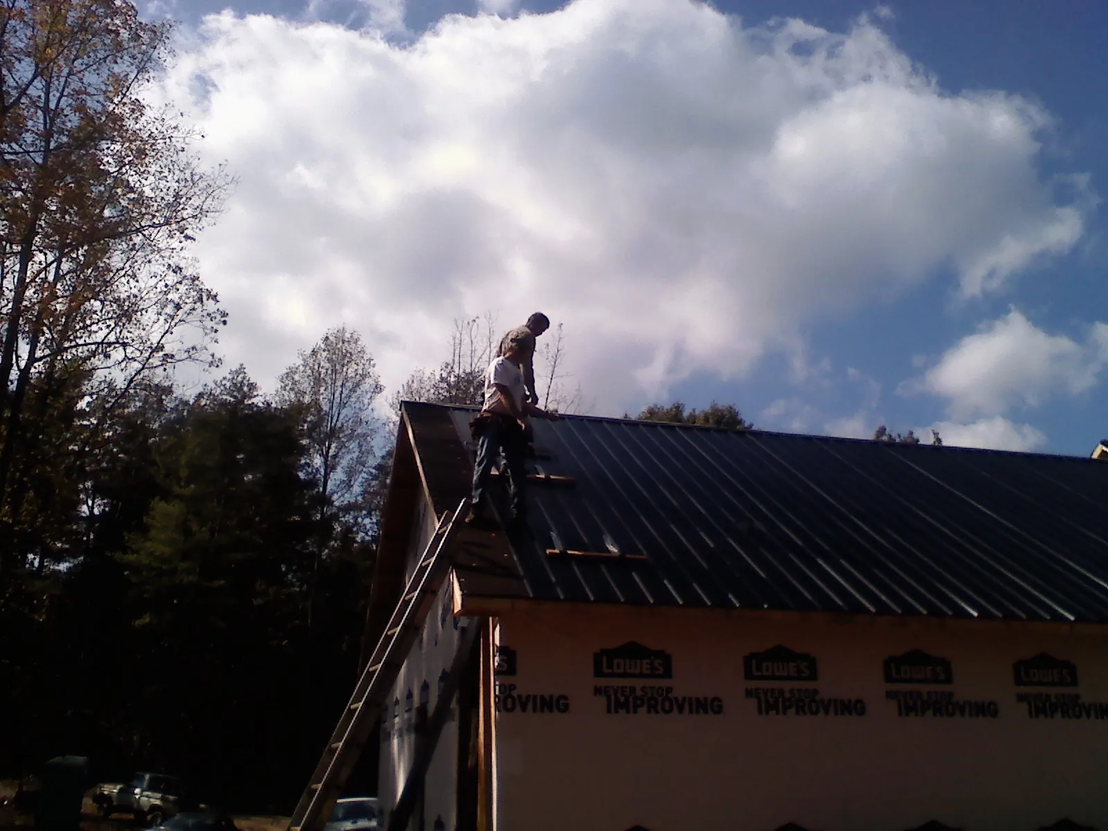 Roofer fastening dark metal panels high against a cloudy sky, from a Roof Inspection job in Irwin